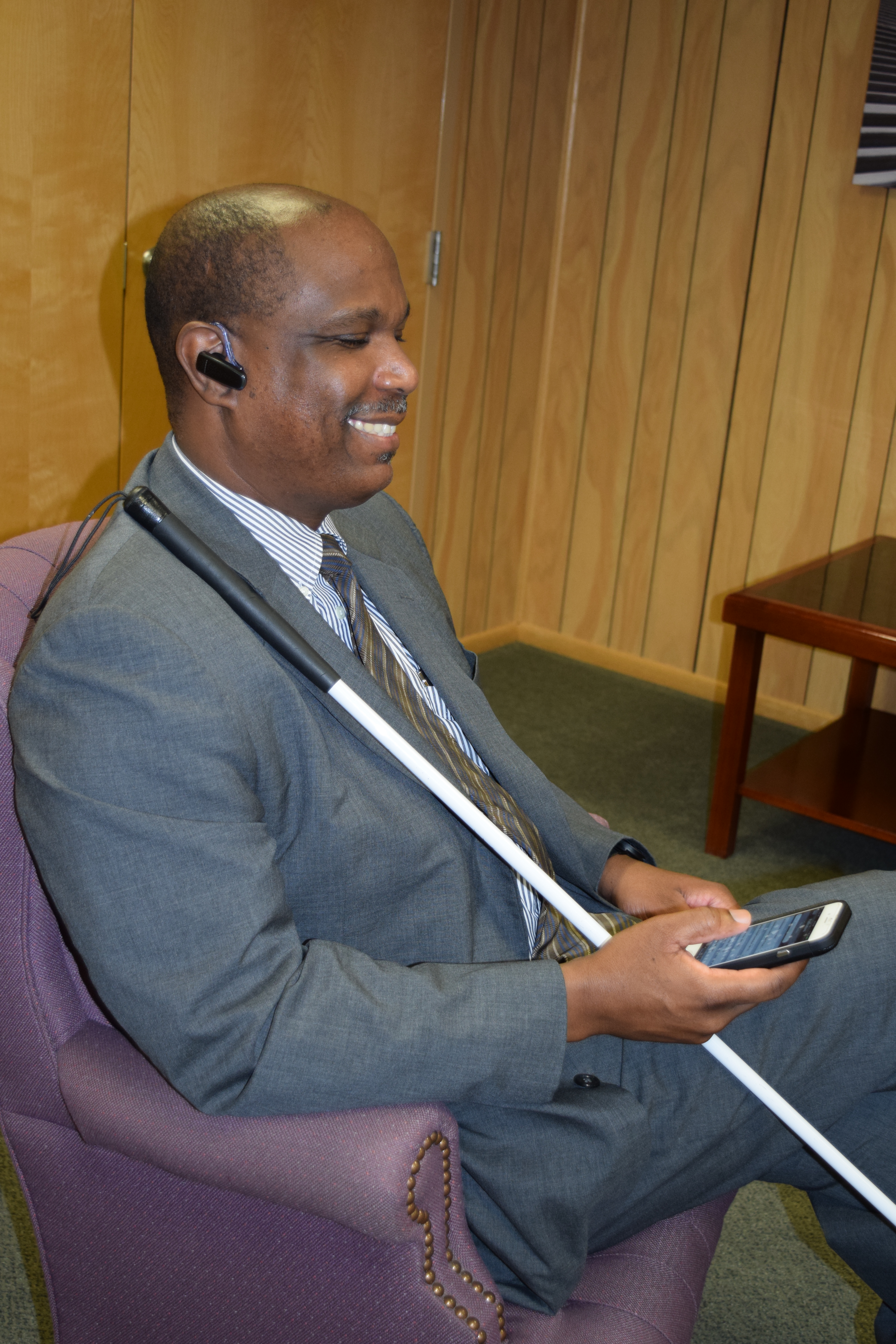 Anil Lewis using an iPhone with Bluetooth earpiece while sitting in a chair.